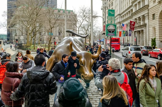 Bull and Bear, Bull Statue Monument at New York Stock exchange with lots of tourist in the forefront taking photos, during winter, horizontal