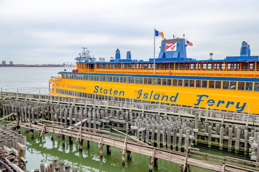 Yellow Staten Island Ferry at the Staten Island Terminal, wood jetty in the forefront, side view, during winter day with overcast, horizontal