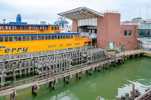 Yellow Staten Island Ferry at Staten Island Terminal, side view, wood jetty in the forefront, during winter day with overcast, horizontal