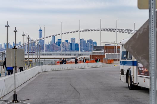 Staten Island Ferry Terminal People walking in line to exit the Terminal, Skyline of Manhattan, New York City in the distance, bus passing by, during winter day with overcast, horizontal