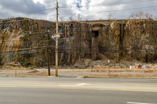 Rock with old wooden electric power pole and road in the forefront, North Bergen, New Jersey, during a sunny winter day, horizontal