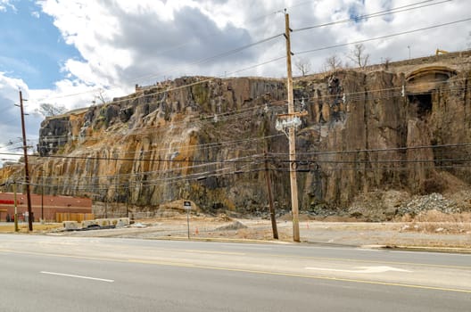 Rock with old wooden electric power pole and road in the forefront, North Bergen, New Jersey, during a sunny winter day, horizontal