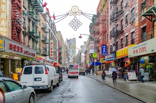 China Town New York City with retail stores and traffic, People walking with umbrella on the sidewalk of the street, parked cars on the street during rainy winter day with overcast, horizontal
