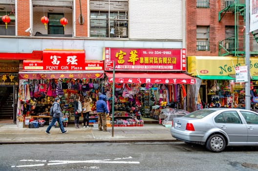 Red FQNY Gift Plaza and New York Souvenir Wholesale & Retail stores at China Town, with people standing in front, car parked next to the store, New York City, during rainy winter day with overcast, horizontal