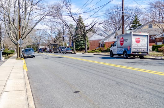 Typical Street in New Jersey with parked cars and delivery vehicle next to the sidewalk of the street during sunny winter day, horizontal