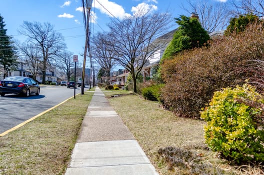 Sidewalk next to a typical Street in New Jersey during a sunny winter day, cars passing by, residential area, horizontal