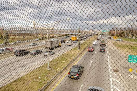 Highway in Queens with metal fence in the front, New York City near Flushing-Meadows-Park during overcast winter day, horizontal