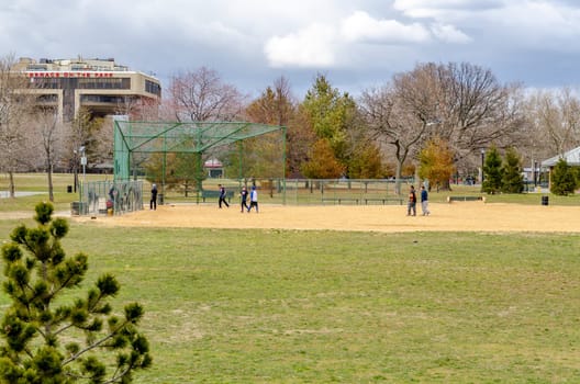 Young male Students playing Baseball in Flushing-Meadows-Park during overcast winter day with Terrace in the Park Restaurant in the background, horizontal