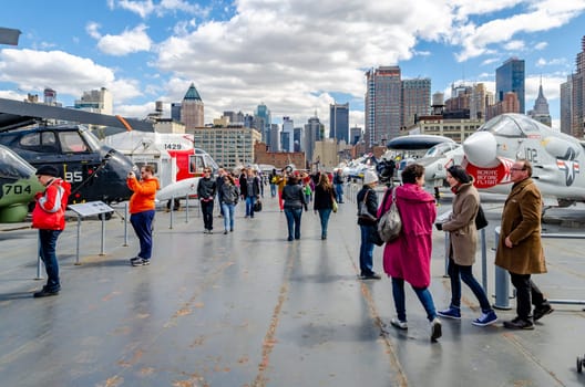 Deck of the Intrepid Sea-Air-Space Museum with lots of fighter jet and helicopter standing, people walking around, New York City during sunny winter day, horizontal