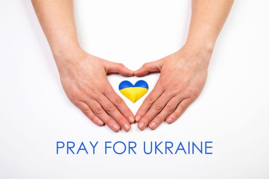 Heart shaped flag of Ukraine in female hands, Pray for Ukraine text.  The concept of solidarity with the citizens of Ukraine.