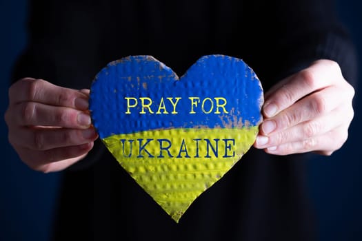 Heart shaped flag of Ukraine in female hands, Pray for Ukraine text.  The concept of solidarity with the citizens of Ukraine.