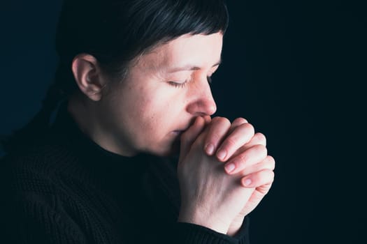 Religious young woman praying to God, on dark background.