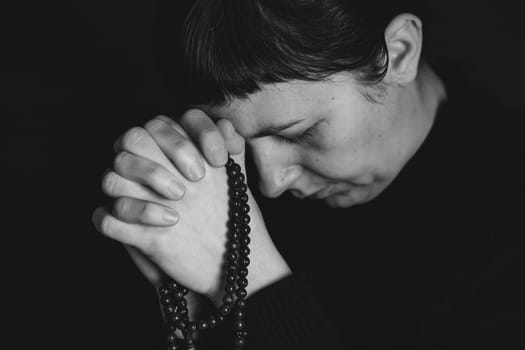 Religious young woman praying to God, on dark background.