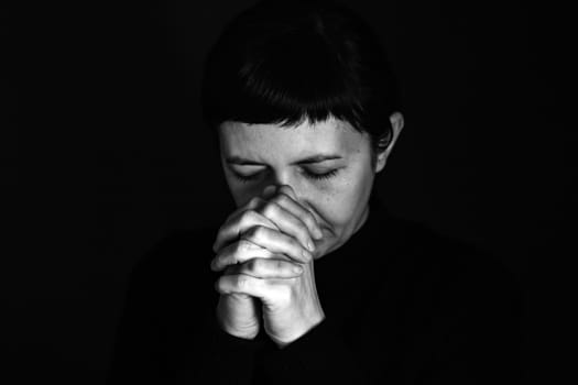 Religious young woman praying to God, on dark background.
