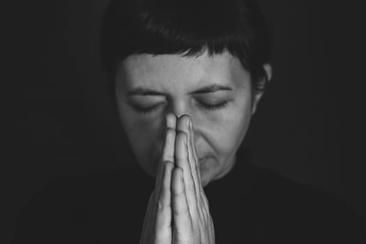 Religious young woman praying to God, on dark background.