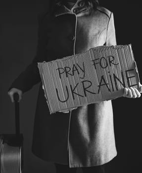 Ukrainian refugee holding placard with Pray for Ukraine text. Evacuation of civilians. Freedom to Ukraine concept.