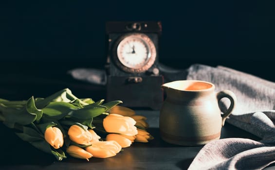 Still life with bouquet of yellow tulip flowers in old vintage jug, in beam of light on dark background.Art photography.