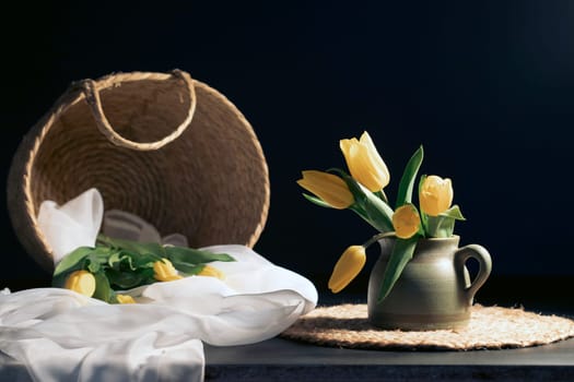 Still life with bouquet of yellow tulip flowers in old vintage jug, in beam of light on dark background.Art photography.