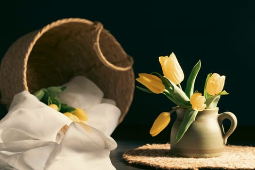 Still life with bouquet of yellow tulip flowers in old vintage jug, in beam of light on dark background.Art photography.