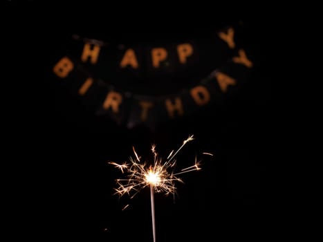Close-up of sparkler on black isolated background with inscription Happy Birthday in golden letters. Footage is shot in 4k from a tripod under artificial professional lighting