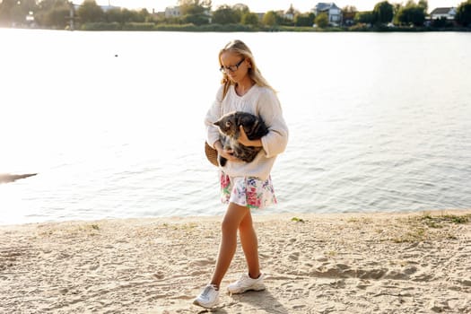 Young blonde, woman, girl walking on the beach in spring in a dress and white sweater with a cat on a sunny day