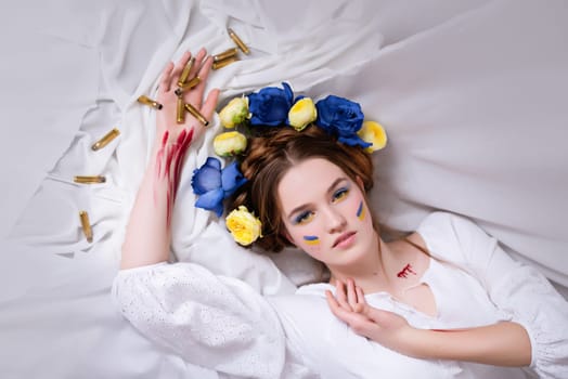 A young Ukrainian woman during the war with a yellow blue wreath of bullets and blood on a white background close-up. Russia attacked Ukraine in 2022