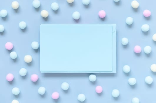 Blank card between pastel pom-poms on light blue top view. Romantic scene with blank horizontal card with place for text flat lay. Spring or boyish concept