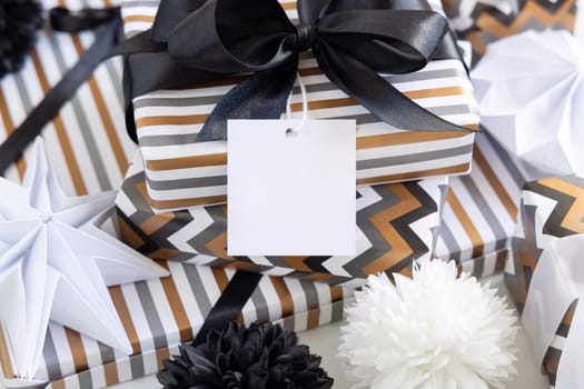 Present with blank square gift tag and black bow close up. Gift boxes wrapped in Striped and chevron geometric paper near black and white decor. Christmas, New Year, Birthday, Anniversary label mockup