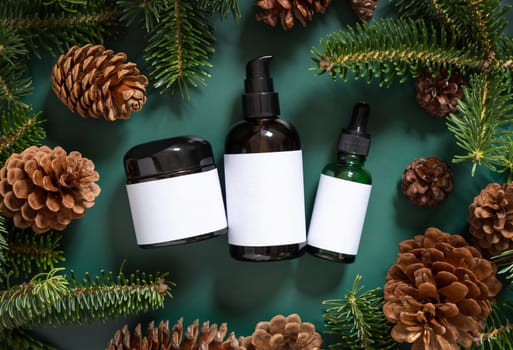 Brown glass jars near fir branches and pine cones on dark green top view. Brand packaging mockup. Skincare beauty product, cream or serum. Healthcare natural cosmetics concept