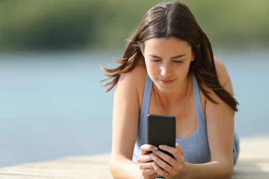 Woman using mobile phone lying on pier