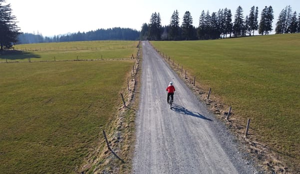 Aerial drone shot of female cyclist on lonely road with shadow