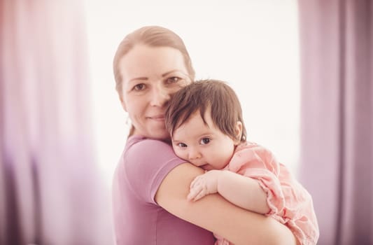 Mother holding in her hands cute daughter indoors. Concept of motherhood.
