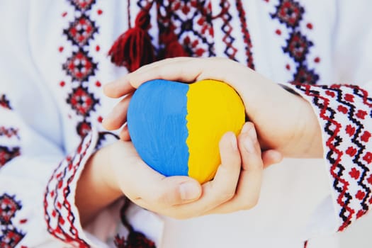 Small little girl in national traditional embroidery or embroidered shirt hold stone heart shape with Ukrane national flag. Love native country and people. Pray for Ukraine piece. High quality photo