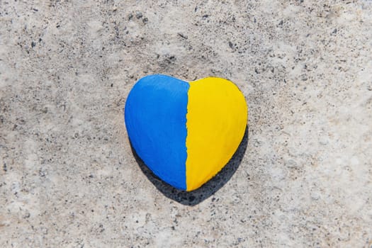 Stone in shape of a heart painted with the Ukrainian flag lies on the ground or concrete. No war. Stop the war, the genocide of Ukrainians. Flat lay with copy space. Save Ukraine people from invasion.