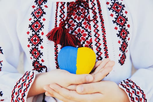 Small little girl in national traditional embroidery or embroidered shirt hold stone heart shape with Ukrane national flag. Love native country and people. Pray for Ukraine piece. High quality photo