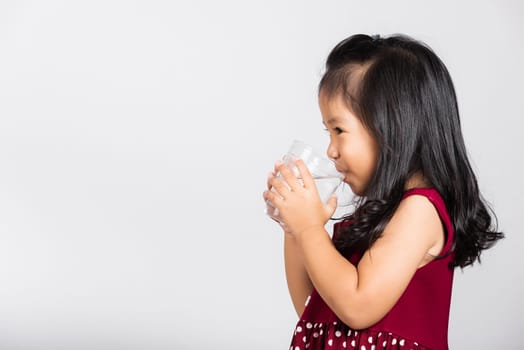 Little cute kid girl 3-4 years old smile drinking fresh water from glass in studio shot isolated on white background, Asian children preschool, Daily life health
