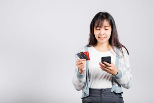 Woman excited smiling hold mobile phone and plastic debit credit bank card for payment studio shot isolated white background, happy young female using smartphone buy and pay online shopping