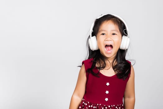 Little cute kid girl 3-4 years old listen music in wireless headphones in studio shot isolated on white background, happy Asian children smiling listening audio, entertainment lifestyle