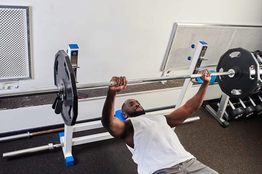 An African American man does a bench press lying on a bench in the gym. High quality photo