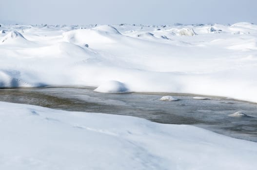 Stunning view of the frozen river covered with chunks of ice and white frosted snow. Snowy desert. The river breaks through the ice.