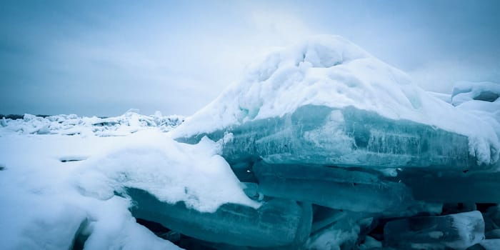Stunning view of the frozen river covered with chunks of ice and white frosted snow. Snowy desert. The river breaks through the ice.