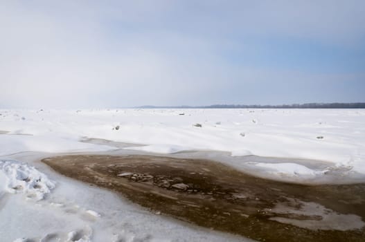 Stunning view of the frozen river covered with chunks of ice and white frosted snow. Snowy desert. The river breaks through the ice.