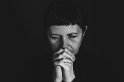 Religious young woman praying to God, on dark background.