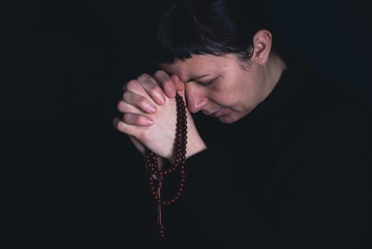 Religious young woman praying to God, on dark background.