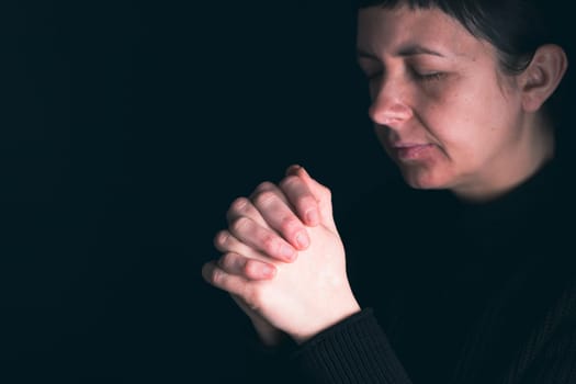 Religious young woman praying to God, on dark background.