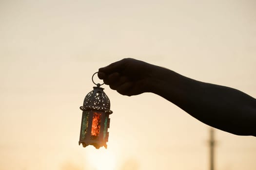 Ramadan Kareem background. Hand holding ornamental Arabic lantern in the sunset
