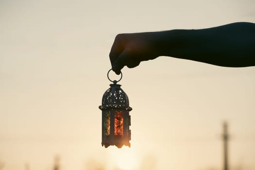 Ramadan Kareem background. Hand holding ornamental Arabic lantern in the sunset