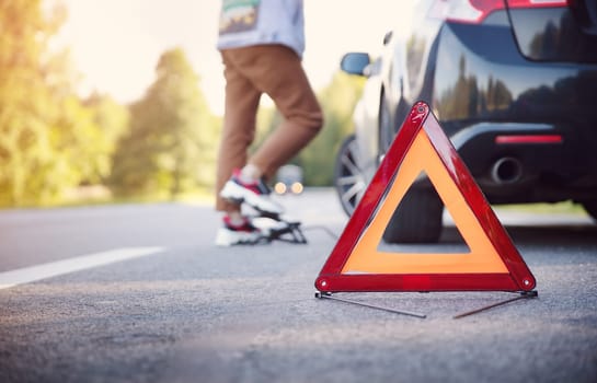 Woman pumping up the wheel of the car on the roadside of the street. Red triangle on the highway.