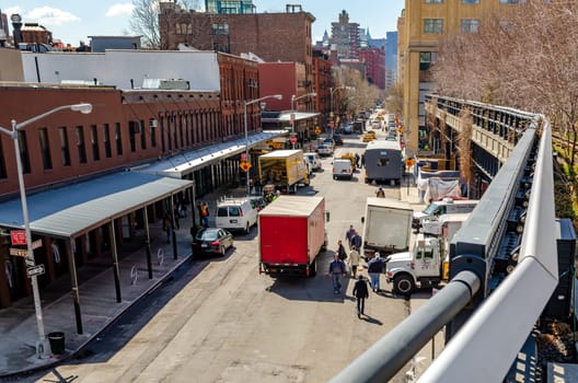 City Street in Chelsea with lots of traffic, trucks parked on the street, view from the High Line Rooftop Park with fence in front, New York City during sunny winter day, horizontal