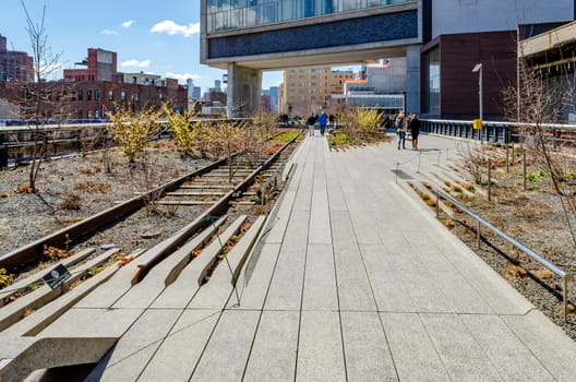 People walking at the High Line Rooftop Park, New York City way with railroad track next to it during sunny winter day, horizontal